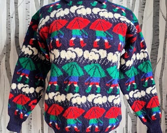 May include: A blue, white, red and green knitted jumper with a pattern of umbrellas and people wearing boots. The jumper has a crew neck and long sleeves.