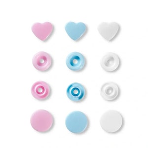 Könnte beinhalten: Sortiment aus Plastik-Druckknöpfen in Rosa, Blau und Weiß. Die Druckknöpfe sind in Form von Kreisen und Herzen.