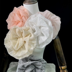 Peut inclure: Un ensemble de quatre grands accessoires de cheveux circulaires en tissu avec une texture scintillante et pailletée. Le lot comprend une pièce pêche, une blanche, une crème et une gris foncé, chacune avec un design froncé et volanté.