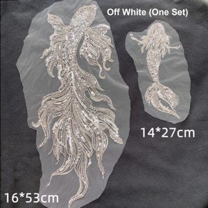 Puede incluir: Apliques de pez y sirena con cuentas de color blanco roto. El aplique de pez mide 16 x 53 cm, y el aplique de sirena mide 14 x 27 cm. Los apliques están adornados con lentejuelas y cuentas, y están sobre un respaldo transparente.