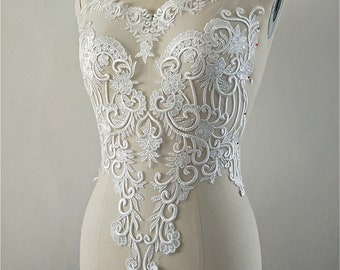 May include: White lace applique with a delicate floral design. The lace is intricate and detailed, with a variety of shapes and sizes of flowers. The applique is perfect for adding a touch of elegance to any project.