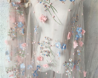 May include: Pink tulle fabric with blue and pink embroidered flowers. The flowers are 3D and have a delicate, feminine look.