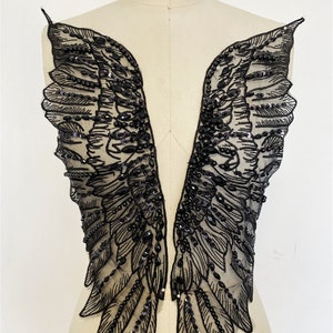 May include: A pair of black beaded angel wings with a sheer mesh fabric. The wings are embellished with black beads and sequins.