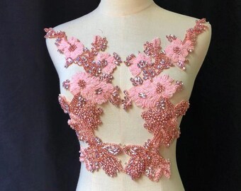 Könnte beinhalten: Zwei rosa Blumenapplikationen mit Strasssteinen und Perlen. Die Applikationen sind perfekt, um jedem Kleidungsstück einen Hauch von Glanz und Eleganz zu verleihen.