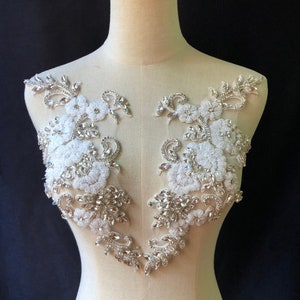 May include: Two white floral appliques with clear rhinestones and beads. The appliques are on a white mannequin bust.