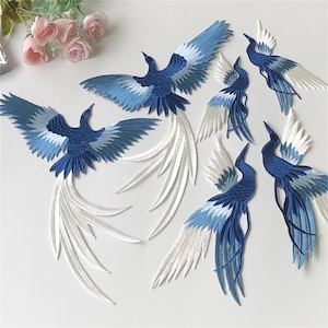 May include: A set of six blue and white embroidered iron-on patches featuring a stylised bird design. The birds have long, flowing tails and are in various poses.