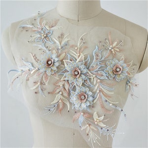 Peut inclure: Une applique florale délicate avec des fleurs, des feuilles et des perles de couleur bleu clair et pêche. L'applique est parfaite pour ajouter une touche d'élégance aux vêtements, aux accessoires ou à la décoration de la maison.
