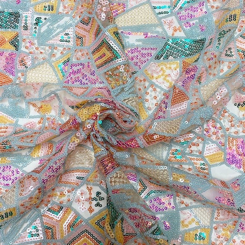 May include: A close-up of a light blue fabric with a geometric pattern of sequins in shades of pink, yellow, orange, and green.