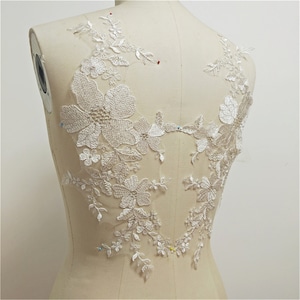 Peut inclure: Applique en dentelle florale blanche avec des fleurs et des feuilles délicates. Cette applique en dentelle est parfaite pour ajouter une touche d'élégance à n'importe quel vêtement.