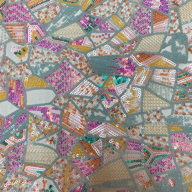 May include: A close-up of a fabric with a geometric pattern made of sequins in shades of pink, teal, gold, and white. The sequins are arranged in a mosaic-like design on a sheer, light-colored fabric.