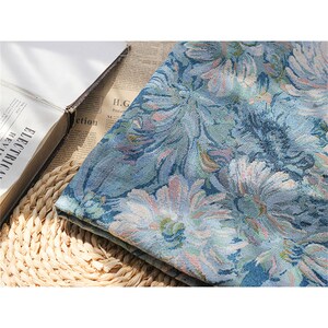 May include: A blue fabric with a floral pattern. The fabric has a textured surface and is woven with a variety of shades of blue, green, and pink.