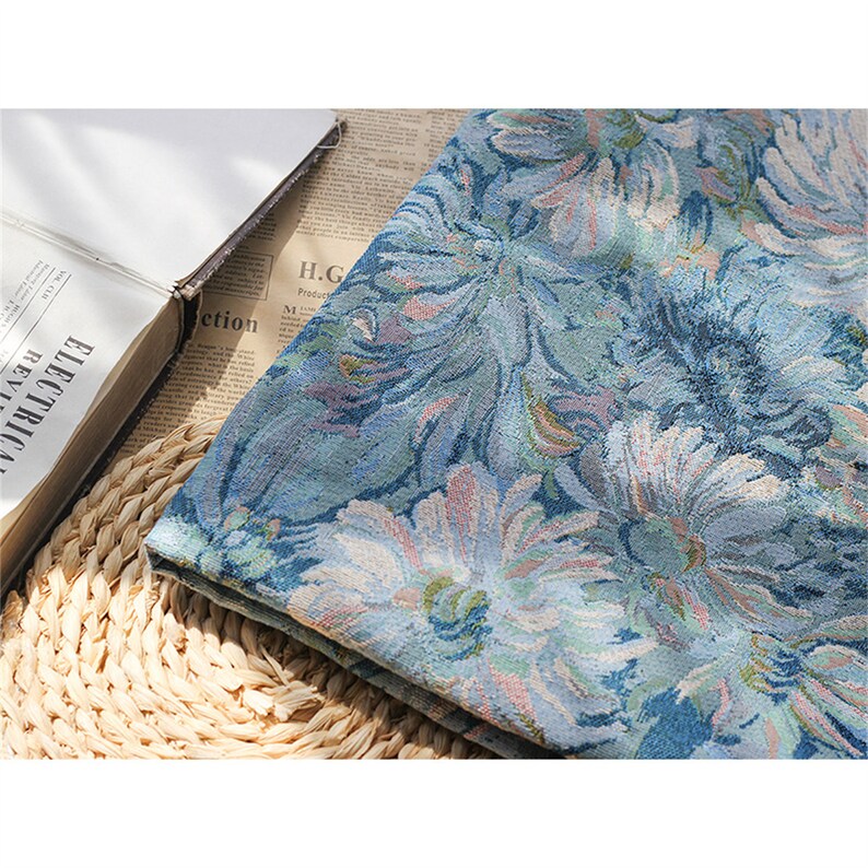 May include: A blue fabric with a floral pattern. The fabric has a textured surface and is woven with a variety of shades of blue, green, and pink.
