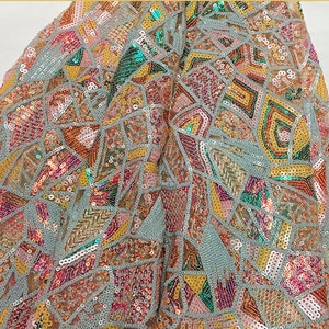 May include: A close-up of a light blue fabric with a geometric pattern of sequins in shades of pink, yellow, green, and orange.