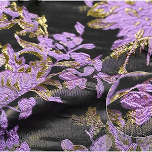 May include: Purple and gold floral brocade fabric with a textured, raised design. The fabric has a shiny, metallic finish.