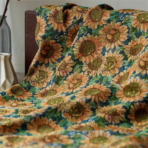 May include: A tapestry throw blanket with a sunflower pattern. The blanket is made of a soft, woven fabric and features a blue background with yellow and brown sunflowers.