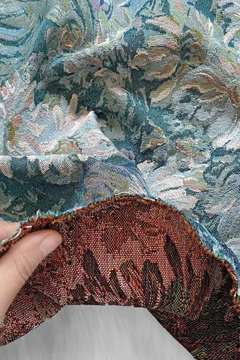 May include: Close-up of a teal and cream floral tapestry fabric with a brown and black woven backing. The fabric is folded over to show the backing.