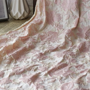 May include: Pink and white floral fabric with a textured, raised design. The fabric has a soft, delicate feel.