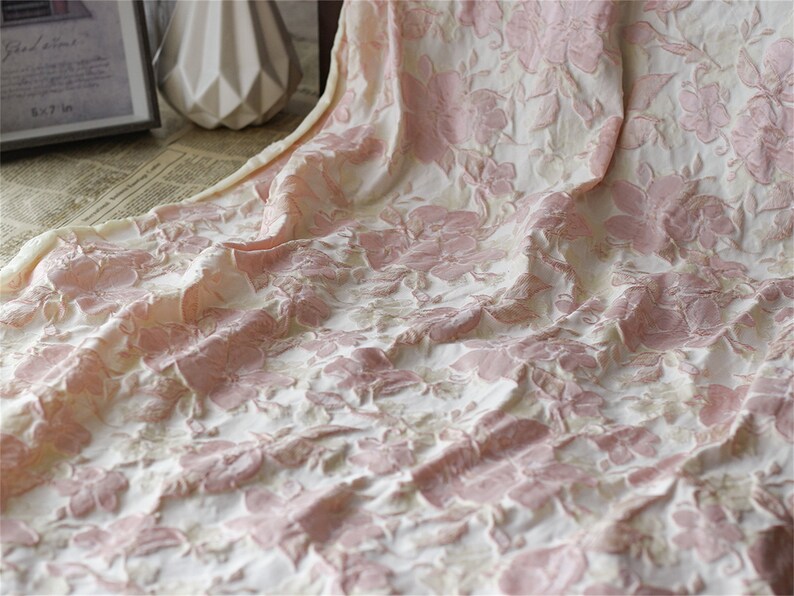 May include: Pink and white floral fabric with a textured, raised design. The fabric has a soft, delicate feel.