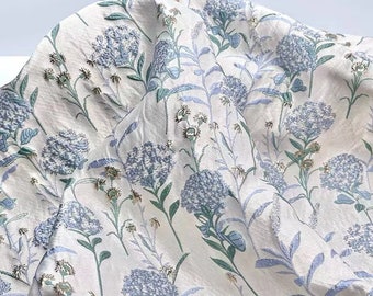 May include: White fabric with a blue floral pattern. The fabric has a raised texture, giving it a 3D effect.