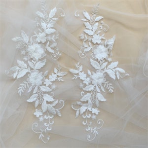 May include: Two white floral lace appliques with delicate flower and leaf designs. The appliques are perfect for adding a touch of elegance to clothing, accessories, or home decor projects.