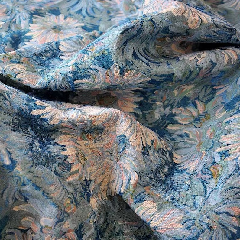 May include: Blue and white floral fabric with a textured, woven design. The fabric is folded and draped, showing the pattern and texture.