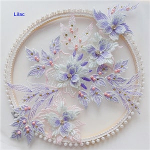 May include: Lilac floral lace applique with pearl and rhinestone embellishments. The applique is on a white background and is surrounded by a circle of pearls.