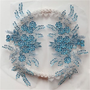 Może przedstawiać: Dwa niebiesko-białe aplikacje kwiatowe z cekinami i koralikami. Aplikacje znajdują się na białym tle i idealnie nadają się do dodania odrobiny elegancji do każdego projektu.