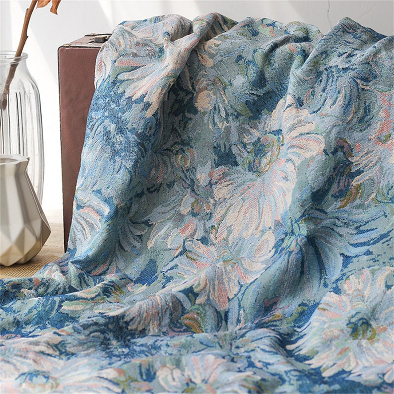 May include: A blue and white floral patterned fabric with a soft, textured surface. The fabric is folded and draped over a brown surface.