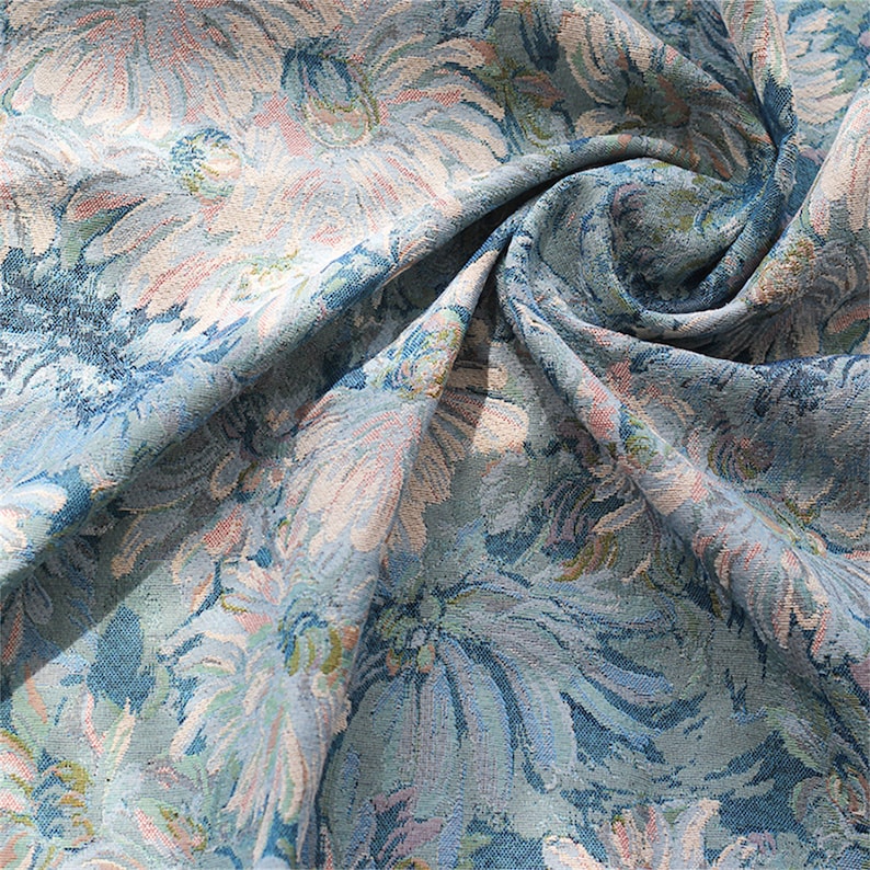 May include: A blue and white floral fabric with a textured, woven design. The fabric is folded and draped, showing the pattern and texture.