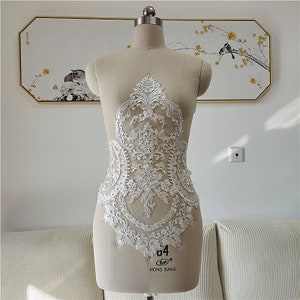 May include: White lace applique with a floral design. The applique is displayed on a dress form.