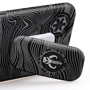 May include: A black phone case with a grey woodgrain pattern and a white kickstand. The kickstand features a Mandalorian symbol and the text "This is the way".