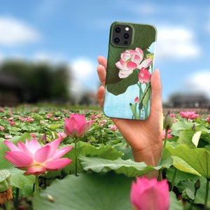 May include: A phone case with a floral design featuring pink lotus flowers and green leaves. The case is designed for a phone with a camera bump and has a black border.