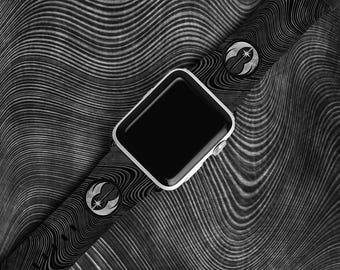 May include: A black and white smartwatch with a patterned band. The watch has a silver case and a black screen. The band features a repeating pattern and silver accents. The watch is displayed on a textured surface.