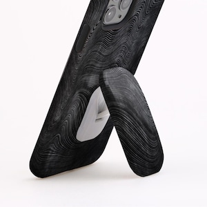 May include: A black phone case with a wood grain pattern and a built-in kickstand. The phone case is designed to prop up the phone for hands-free viewing.