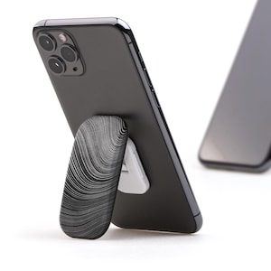 May include: Two black smartphones with a white stand. The stand is a small, foldable, and textured piece that allows the phone to stand upright.