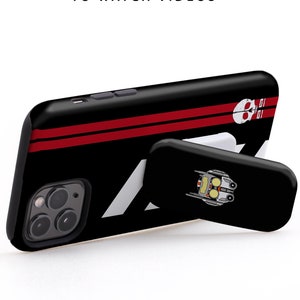 May include: Black phone case with a red stripe and a skull graphic. The case has a white kickstand with a robot graphic. The text "USE IT IN LANDSCAPE MODE TO WATCH VIDEOS" is visible above the phone case.
