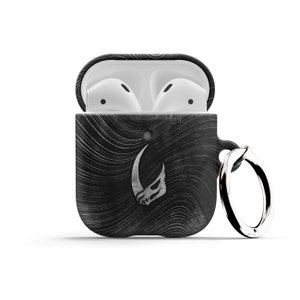 May include: Black and white patterned Airpods case with a silver Mandalorian symbol and a silver keychain ring.