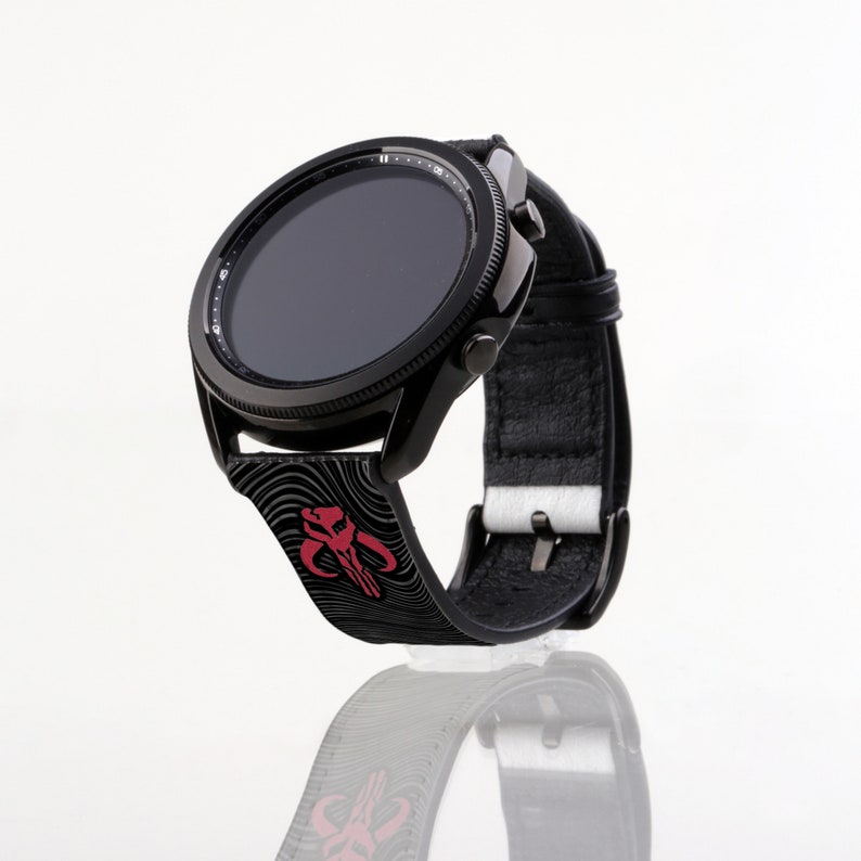 Op de afbeelding: Zwarte smartwatch met een rood en zwart Mandalorian-symbool op de band. Het horloge heeft een zwart wijzerplaat met witte markeringen.