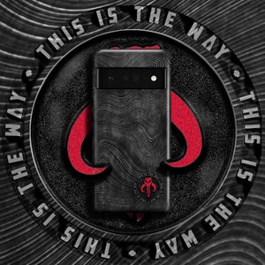 May include: A black phone case with a textured design and a Mandalorian symbol. The case has the text "This is the way" repeated around the edge.