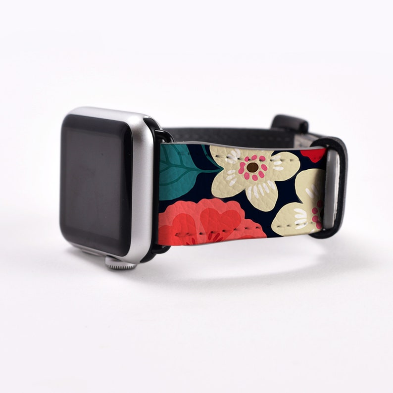Op de afbeelding: Een zwarte Apple Watch met een band met bloemenprint. De band heeft roze, witte en groene bloemen op een donkerblauwe achtergrond.