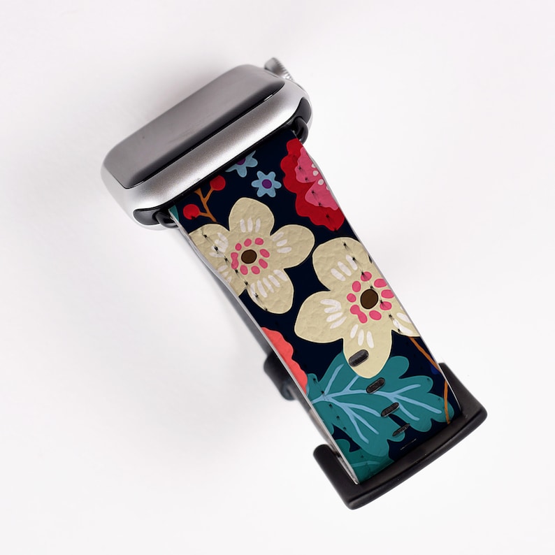 Op de afbeelding: Een zwart-witte bloemenband met een zilveren horloge. De band heeft een donkerblauwe achtergrond met witte en roze bloemen en groene bladeren.