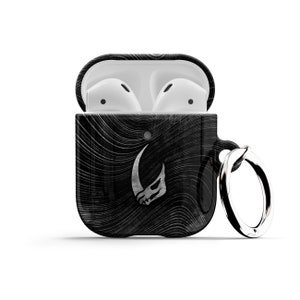 May include: Black and white patterned Airpod case with a silver Mandalorian symbol and a silver keychain ring.