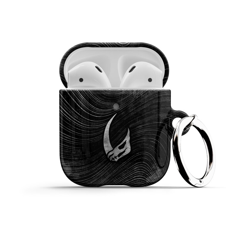 May include: Black and white patterned Airpod case with a silver Mandalorian symbol and a silver keychain ring.