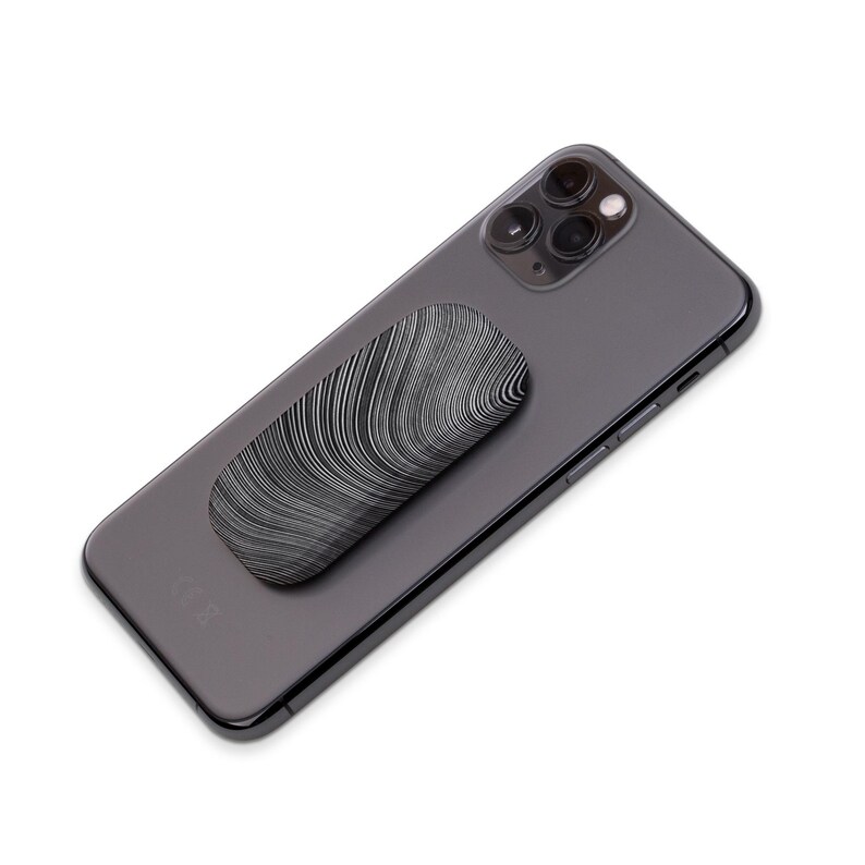 Puede incluir: Un tel&eacute;fono negro con un agarre de tel&eacute;fono estampado en blanco y negro pegado en la parte posterior.