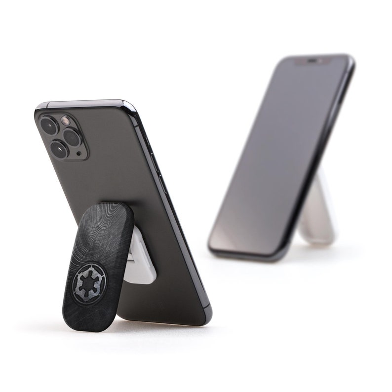 K&ouml;nnte beinhalten: Zwei schwarze Smartphones mit einem dunkelgrauen Holz-Telefonst&auml;nder. Der St&auml;nder zeigt das imperiale Symbol von Star Wars.