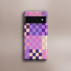 May include: A purple, pink, and cream checkered phone case with a black camera lens.
