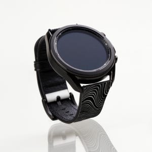 May include: A black smartwatch with a black and white patterned band. The watch face is black and has a circular design.