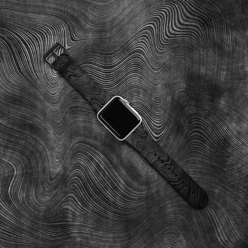 May include: A black smartwatch with a black and white patterned band. The watch is lying on a black and white patterned surface.