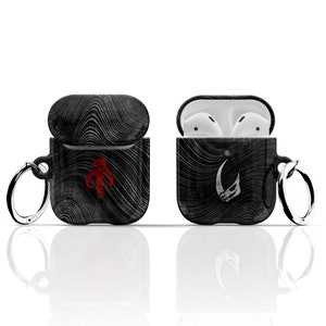 May include: Black and white patterned AirPod case with a red Mandalorian symbol on one side and a white Mandalorian symbol on the other side. The case has a silver ring attached to it.