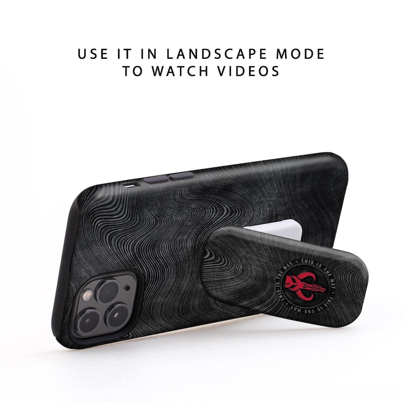 May include: Black phone case with a textured design and a pop-out stand. The stand has a Mandalorian symbol and the text "This is the way."